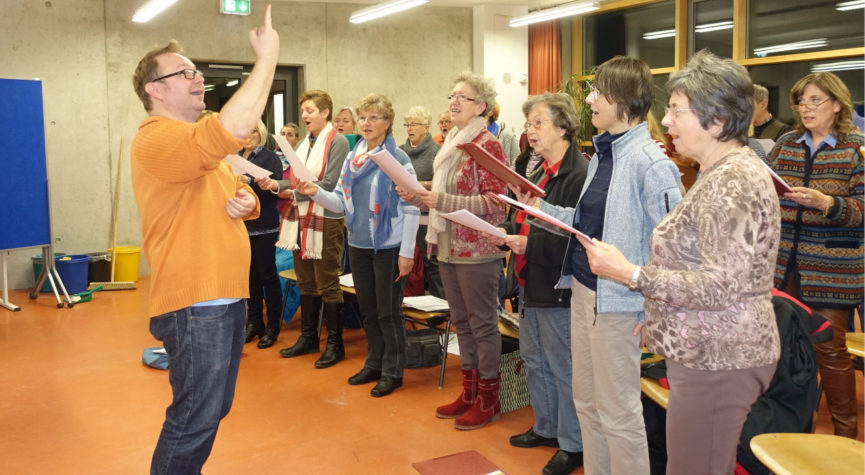Chorleiter demonstriert beim Proben dem Chor mit erhobener Hand